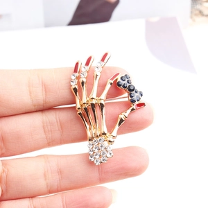 Detail of skull hand brooch with red enamel nails and rhinestone bow decoration