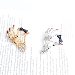 Detail of skull hand brooches with red enamel nails and rhinestone bow on magazine