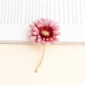 Close-up of pink enamel daisy brooch with gold flower stem on a vintage book