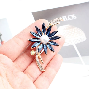 Détail d'une broche fleur en cristal bleu avec perle centrale et placage doré élégant