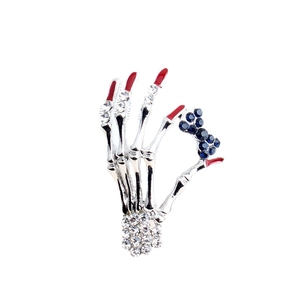 Retro skeleton hand brooch with rhinestones and red fingertips on white background