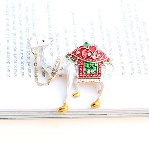 Vue macro d'une broche alpaga en émail blanc avec cristaux colorés et chaîne dorée
