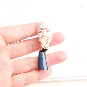 Artistic face mask brooch with dark blue enamel finish and silver pin on hand