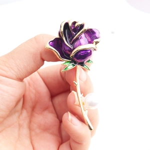 Close-up of purple enamel rose brooch with golden edges, green leaves and a white pearl