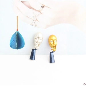 Detailed view of abstract face brooches in gold and silver finish with blue enamel