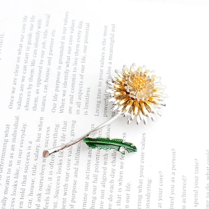 Detailed close-up of a dandelion brooch with gold and silver petals on a white book page
