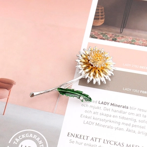 Detail of silver dandelion brooch with gold core, green leaf and rhinestone accent