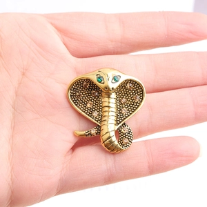 Macro detail of golden cobra brooch featuring green rhinestones and scale texture