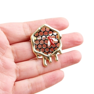 Goldene Bienenwabe Brosche mit rotem Bienendetail und schwarzer Emaille in der Hand