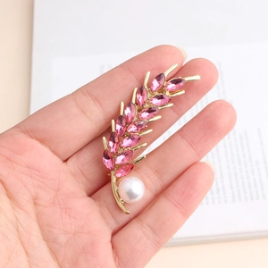 Macro detail of wheat ear brooch with pink crystals and large white pearl on golden metal