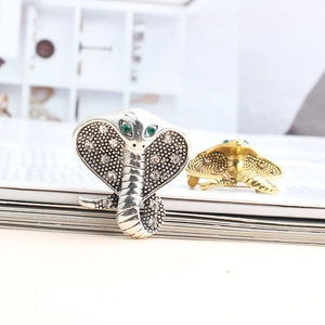 Macro shot of silver and gold cobra brooches with green gemstone eyes and rhinestones