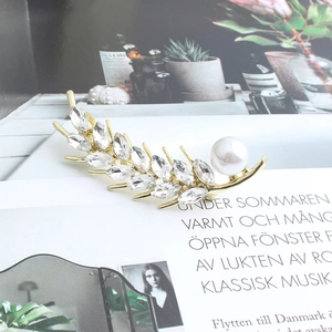 Detail of leaf brooch with marquise crystals and pearl on a magazine page