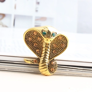 Macro view of gold alloy cobra brooch featuring green crystal eyes and amber rhinestones