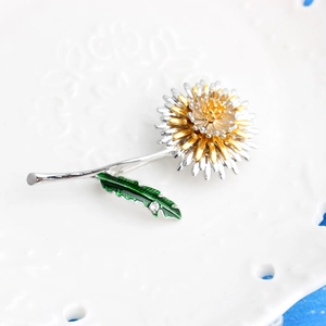 Minimalist dandelion brooch with silver petals and green enamel leaf on a white plate