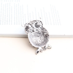 Vintage owl safety pin brooch with silver alloy feather texture on antique book background