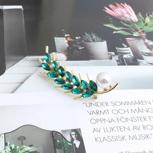 Detail of a gold wheat brooch with green crystals and a white pearl on a magazine