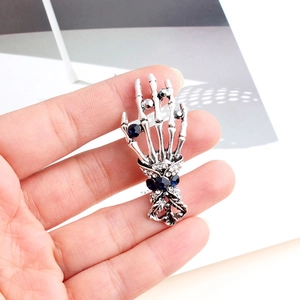Detailed view of a vintage silver skull hand brooch with deep blue crystals and rhinestones
