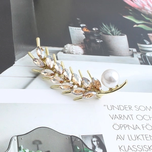 Detail of wheat ear brooch featuring champagne crystals and a white pearl accent