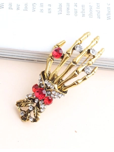 Detailed close-up of gothic skeleton hand brooch in antique gold with red and white crystals