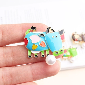 Close-up of a blue cow enamel brooch with colorful hearts and a white pearl accent