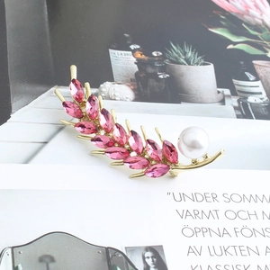 Detailed view of pink crystal wheat ear brooch with imitation pearl on magazine background