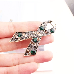 Detailed macro of gold ribbon brooch with green emerald stones and champagne crystals