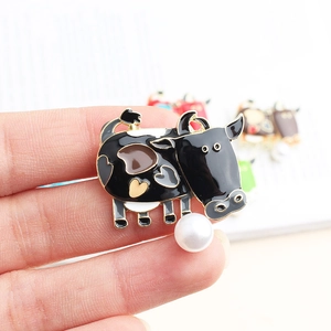 Enamel cow brooch with heart patterns and a white pearl detail held by hand