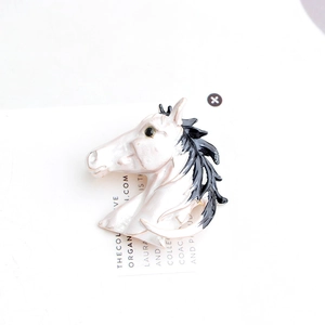 Detail of vintage enamel horse head brooch in cream white with black mane on display card