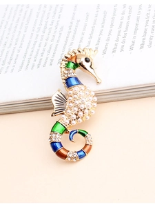 Détail de la broche hippocampe avec émail coloré et perles posée sur un livre ancien