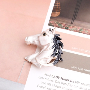 Detail view of a white enamel horse head brooch with black mane on a pink background