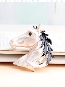Detail of vintage horse head brooch with white enamel finish on an open book background