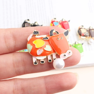 Detailed close-up of a colorful enamel cow brooch with a dangling white pearl charm