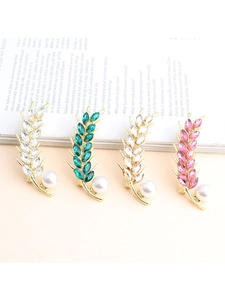 Detailed close-up of four wheat-shaped brooches with colorful gems and pearls on vintage book
