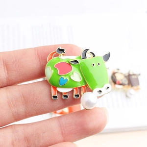 Macro detail of cartoon cow enamel brooch featuring heart patterns and white faux pearl