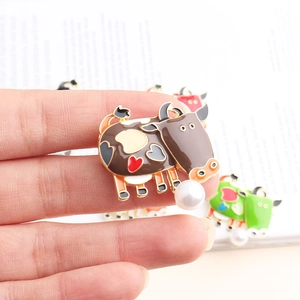 Detailed view of enamel cow brooch with heart pattern and white imitation pearl drop