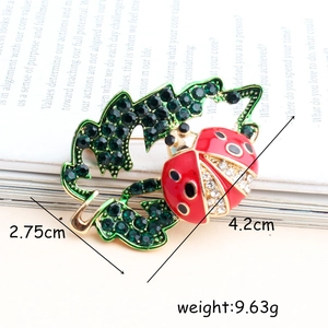 Broche de mariquita en hoja verde con diamantes de imitación y esmalte en un libro