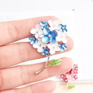 Close-up of enamel flower brooch with rhinestones held in hand for scale
