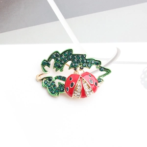 Detalle de broche de mariquita sobre hoja de strass verde con base dorada