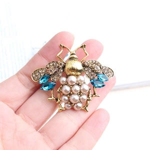 Macro shot of vintage bee brooch with golden base, white pearls and blue crystals