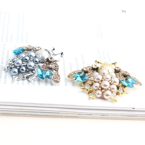 Detailed close-up of bee brooches with blue rhinestones and pearls on a white background