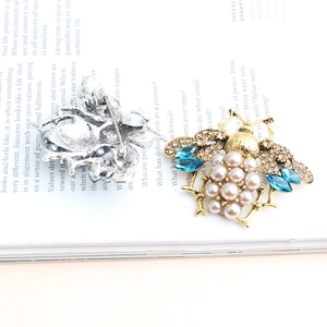 Detailed front and back view of a bee brooch with blue crystals and pearls on a magazine