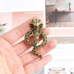 Gros plan d'une broche cobra dorée avec cristaux verts et détails au design exotique