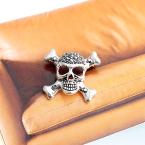 Détail d'une broche crâne vintage en argent avec strass sur surface en cuir brun