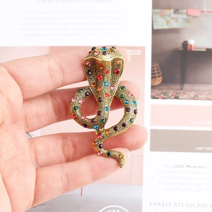 Détail d'une broche serpent en métal doré avec strass colorés tenue à la main