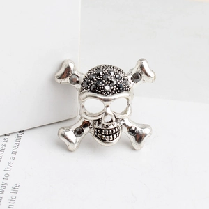 Détail d'une broche crâne gothique argentée avec strass noirs et design d'os croisés