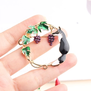 Detail of artistic round fox brooch with enamel grape leaves held by hand