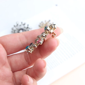Close-up of golden brooch side view with colorful rhinestones held by hand