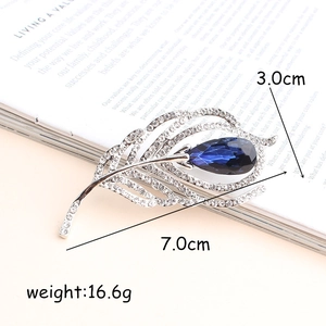 Elegant silver feather brooch with white crystals and a blue teardrop stone on a book