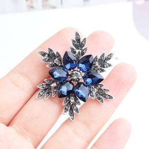 Detailed shot of a snowflake brooch with blue crystals held by hand for size reference