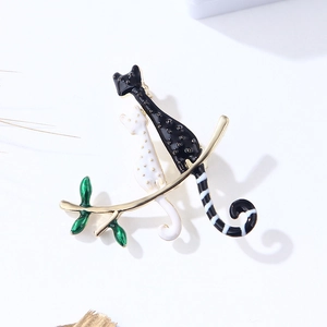 Détail de la broche chat émaillé noir et blanc avec feuilles vertes sur branche